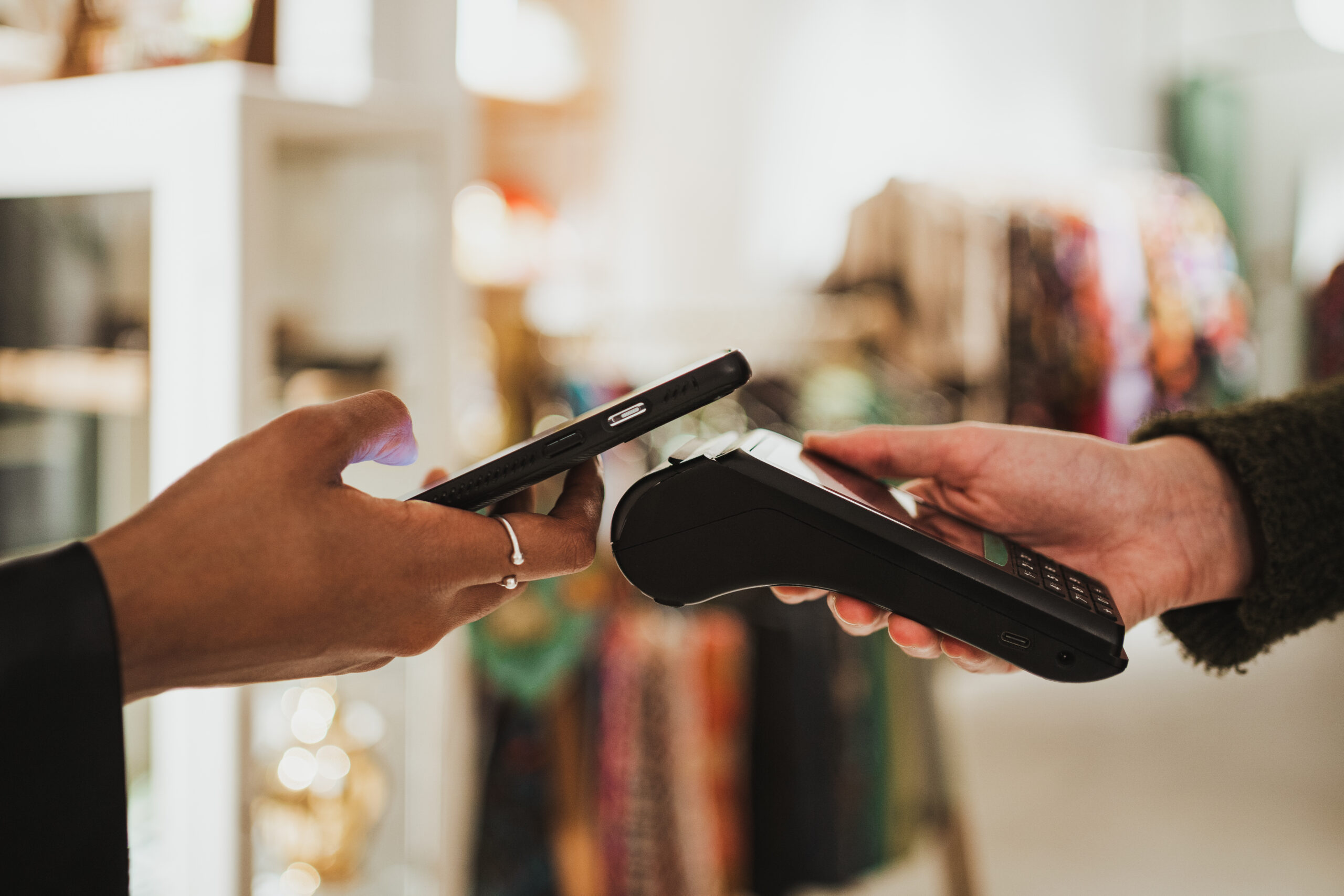 Close up shot of young woman paying contactless on a POS in a shop. She is using her phone